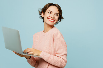 Young IT woman wear beige knitted sweater casual clothes hold use work on laptop pc computer look...