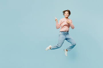 Fototapeta na wymiar Full body side view young happy woman she wear beige knitted sweater casual clothes jump high point index finger aside on area isolated on plain pastel light blue cyan background. Lifestyle concept.
