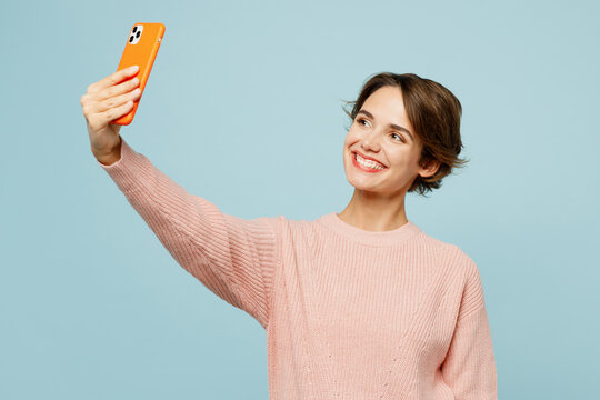 Young woman she wears beige knitted sweater casual clothes doing selfie shot on mobile cell phone post photo on social network isolated on plain pastel light blue cyan background. Lifestyle concept.