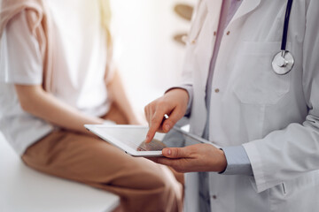 Doctor and patient in clinic. Friendly physician using tablet computer near a young woman. Medicine concept