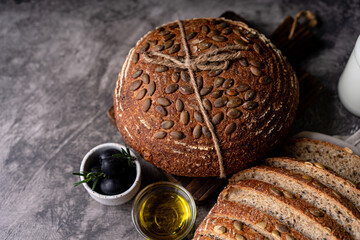 Baked sourdough bread from whole grain flour and pumpkin seeds on a grid, olive oil and black olive on a rustic wooden table. Artisan bread.