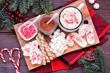 Christmas hot chocolate tray an assortment of sweet toppings. Top view table scene on a dark wood...