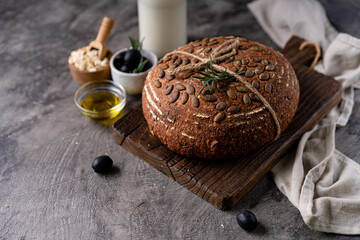 Baked sourdough bread from whole grain flour and pumpkin seeds on a grid, olive oil and black olive on a rustic wooden table. Artisan bread.