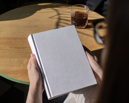 Book cover mock up, hand holding blank clean hardback mockup on wooden desk