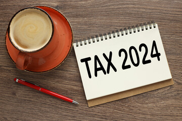 Word Tax 2024 top view on a wooden table. mug and notepad with text
