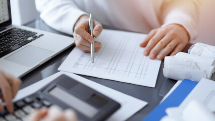 Woman accountant using a calculator and laptop computer while counting taxes for a client. Business audit concepts