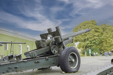 A large artillery military cannon stands on the square, people stand in the distance, green trees