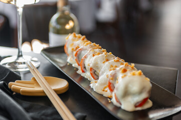 Sushi roll with salmon and vegetables in sauce on a black plate in a restaurant
