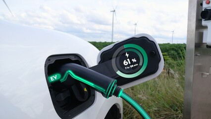 Electric car recharging energy from EV charging station display futuristic smart battery status hologram by EV charger plug cable in wind turbine farm. Alternative clean energy sustainability. Peruse