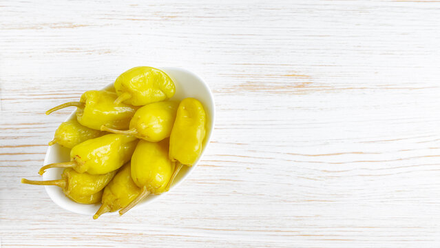 Pickled yellow pepper, pepperoncini or friggitelli in bowl on white wooden background. Hot pepper marinated, brined. Traditional Italian and greek cuisine, ingredient for salad, pasta, sauce.