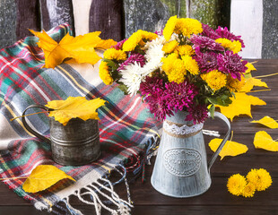 Autumn still life with colorful bouquet of chrysanthemum flowers in vintage vase, vintage cup, pumpkins, yellow autumn leaves, woolen scarf