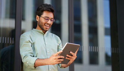 Smiling businessman in eyeglasses use digital tablet standing near office building