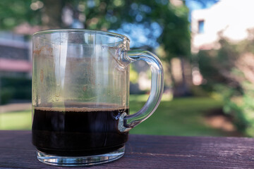 a glass mug with finished coffee in it , on a wooden table in the park