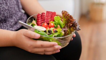 Overweight woman enjoy eating a bowl of vegetable salad at her home.