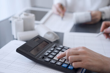 Two accountants use a calculator and laptop computer for counting taxes or revenue balance. Business, audit, and taxes concepts