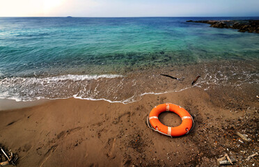 Obraz premium Mediterranean beach, abandoned on the beach an orange ring lifebuoy. Concept of emergency deaths at sea.