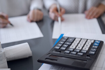 Calculator is waiting to be used while Two accountants are ready to count taxes or make a revenue balance in the background. Business, audit, and taxes concepts