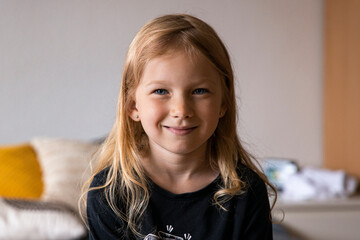 Smiling blonde girl child sitting on the sofa in the room