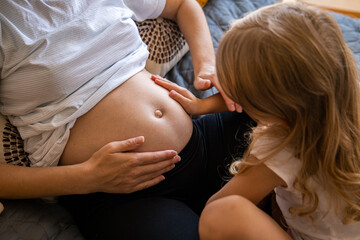 Pregnant young woman with her daughter hold on to her stomach listen to the baby. Top view, flat lay