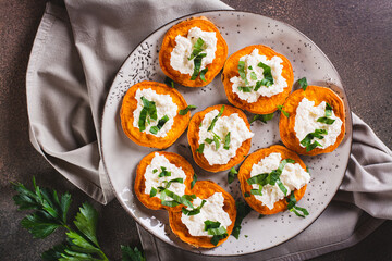 Close up of pieces of baked sweet potato with ricotta and herbs on a plate on the table top view