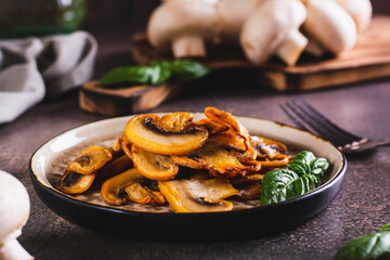 Appetizing fried champignons and basil leaves on a plate on the table