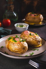 Baked whole potatoes with egg, sausages and herbs on a plate vertical view