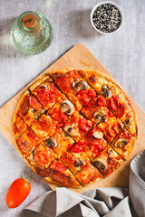American St. Louis Style pizza with bacon, mushrooms and tomatoes on a board top and vertical view