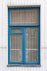 The wooden rectangular window is painted blue. With a metal grill on the glass.