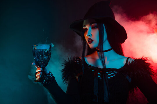 Photo of stunning evil witch lady prepare magical liquid dark potion in goblet over mist neon background