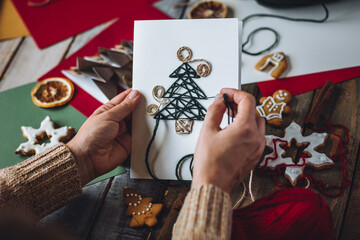 Woman creating handmade craft paper christmas card with wool thread fir tree. Idea for quality...