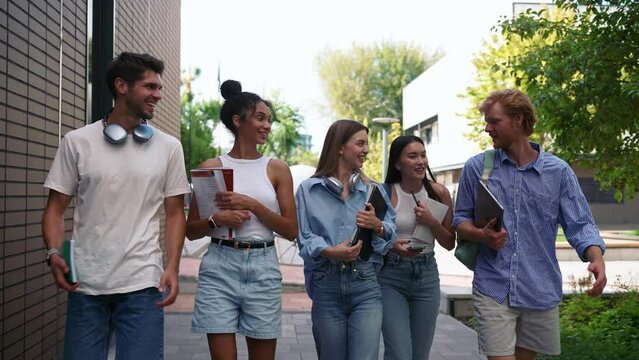 Group of cheerful multinational young students talking and walking near university in summertime