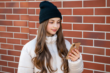 smiling teen girl messaging on phone outdoor. teen girl messaging on phone wearing hat.