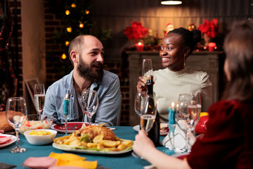 Young person raising glass for speech during christmas eve holiday at home, gathering with friends and family to eat traditional homemade food and give toast at table. Festive people.