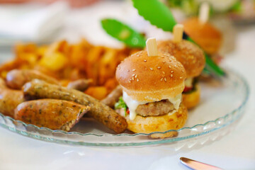 Mini burgers on a plate with french fries and sausages. 