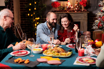 Cute couple meeting family at dinner on christmas eve holiday, gathering around table with persons to eat food and drink wine. Young adults talking to relatives during december event at home.