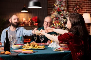 Poster People eating festive food at dinner, celebrating christmas eve together and passing meal plates around the table. Happy family meeting at home to celebrate xmas holiday event, party feast. © DC Studio