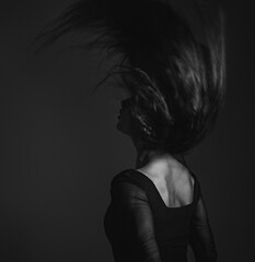 Silhouette of beautiful woman with sporty slim figure in black dress moving with hair above the head on dark shadow art background. Closeup