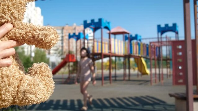 Missing child with teddy toy on playground. A view of person call the child with teddy bear on the playground. A concept of kidnapping problems in the city.