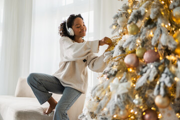 Merry Christmas. African American woman wearing headphones listening music decorating Christmas...