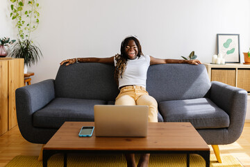 Young african woman having fun watching online videos on laptop at home. Technology and domestic lifestyle concept. - obrazy, fototapety, plakaty