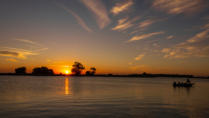 Fishing in boat in silhouette at sunrise on the river