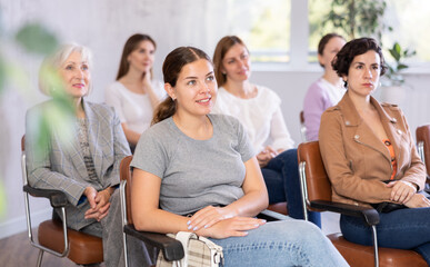 Young smiling woman in casual clothes listening to speaker lecture while sitting in office