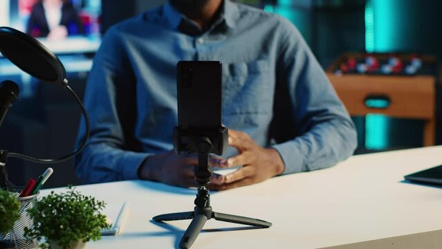 Close up shot of smartphone on holder used by content creator in dimly lit home studio to film video for online streaming platforms. Mobile phone being used by influencer to record footage