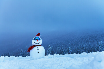Funny snowman in ski glass and red Santa's hat in snowy mountains. Ski resort concept. Merry Christmass and happy New Year