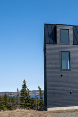 The exterior of a grey and black colored modern pvc or vinyl siding corner wall of a building. The sloped roof is black metal. The windows are single glass panes.