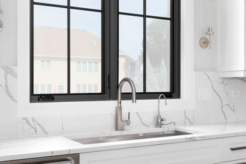 A luxury kitchen faucet detail with white cabinets, white marble countertop and backsplash, and...