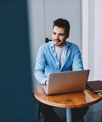 Positive thoughtful male blogger sitting at desktop with laptop device
