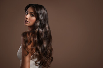 Gorgeous woman with shiny wavy hair on brown background, space for text. Professional hairstyling