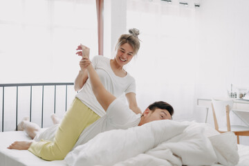 Obraz premium Funny asian couple wife giving husband hurt massage in white bedroom.