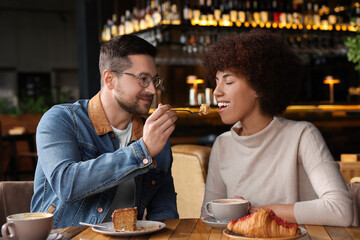 International dating. Beautiful woman feeding her boyfriend with cake in cafe